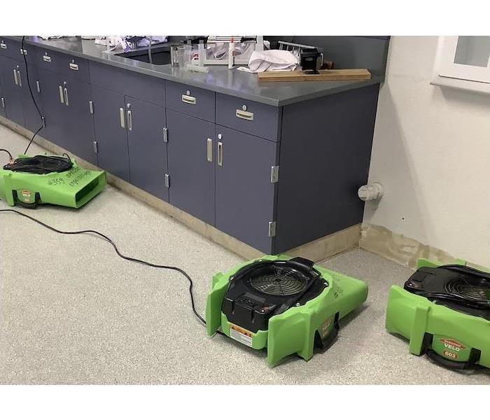 Classroom with air movers drying around a cabinet and wall